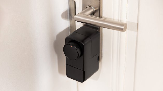 Smart lock attached to a door handle with a round rotary knob and a small red indicator.