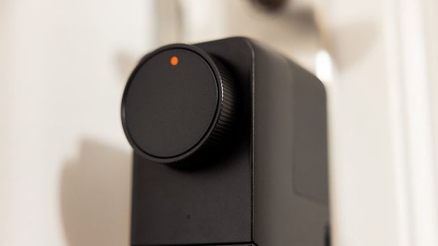 Close-up of a SwitchBot Lock Pro device with a round button and an orange indicator light.