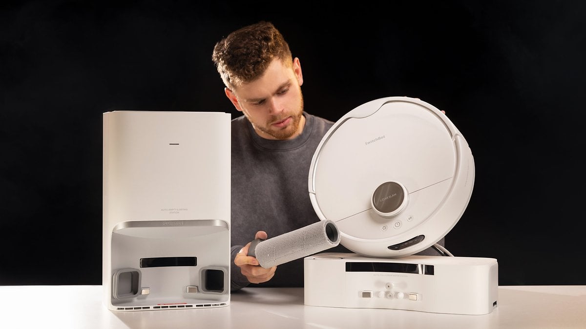 Un homme examine l'aspirateur robot SwitchBot S10 et sa station d'accueil.