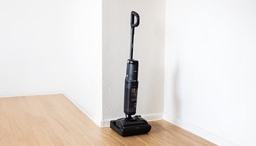 A Tineco Floor One S7 Stretch vacuum cleaner stands in a corner of a room on a wooden floor.