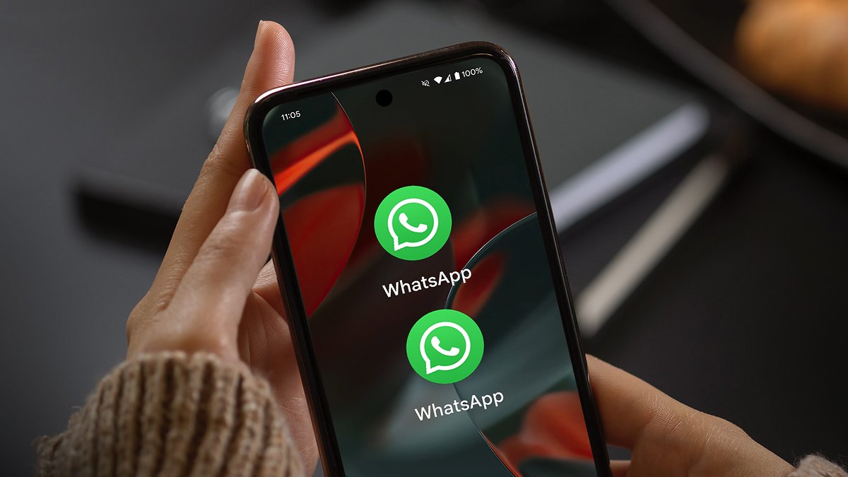 Une main tenant un smartphone affichant l'icône de l'application WhatsApp deux fois à l'écran.