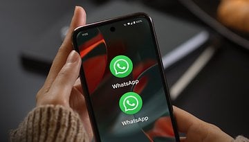 A hand holding a smartphone displaying the WhatsApp app icon twice on the screen.