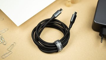 A Ugreen 140W charger with a black USB-C cable coiled next to it on a beige surface.