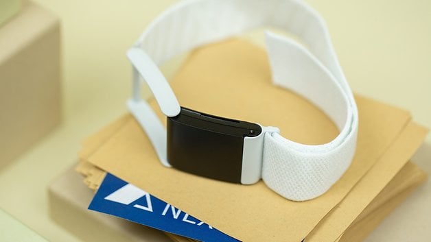 A black fitness tracker with a white strap on a stack of envelopes and a blue card.