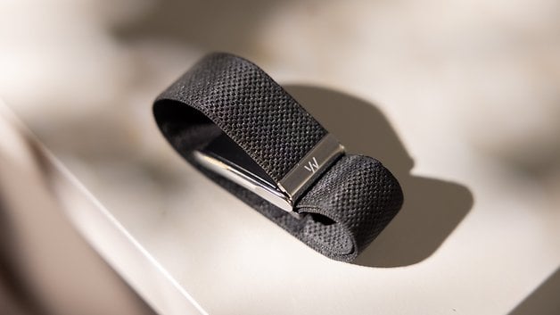 A black textured strap with a silver clasp, resting on a light surface.