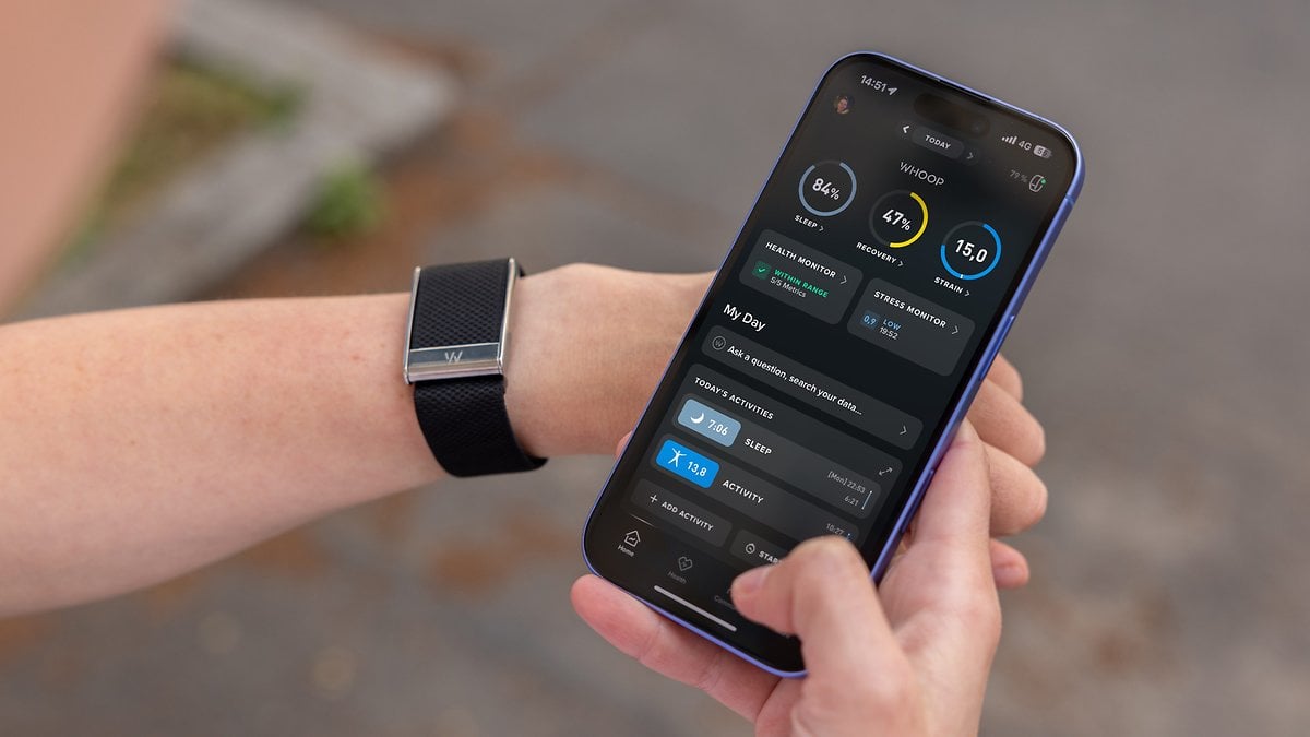 Une personne tenant un smartphone affichant l'application Whoop, avec un tracker de fitness à son poignet.