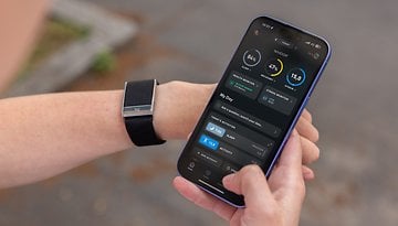 A person holding a smartphone displaying the Whoop app, with a fitness tracker on their wrist.
