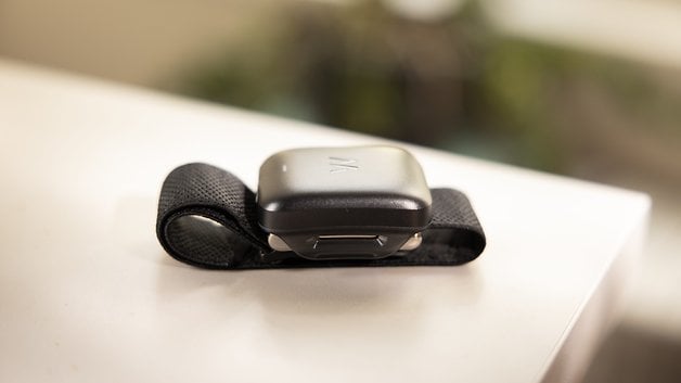 A black wearable device with a strap, resting on a white surface.