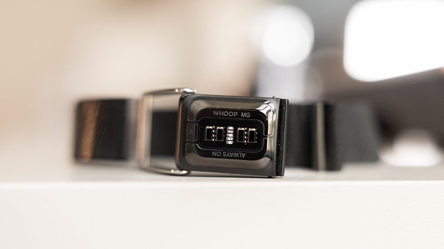 A close-up of a black wearable device displaying 'WHOOP MG' and 'NO' on its front.