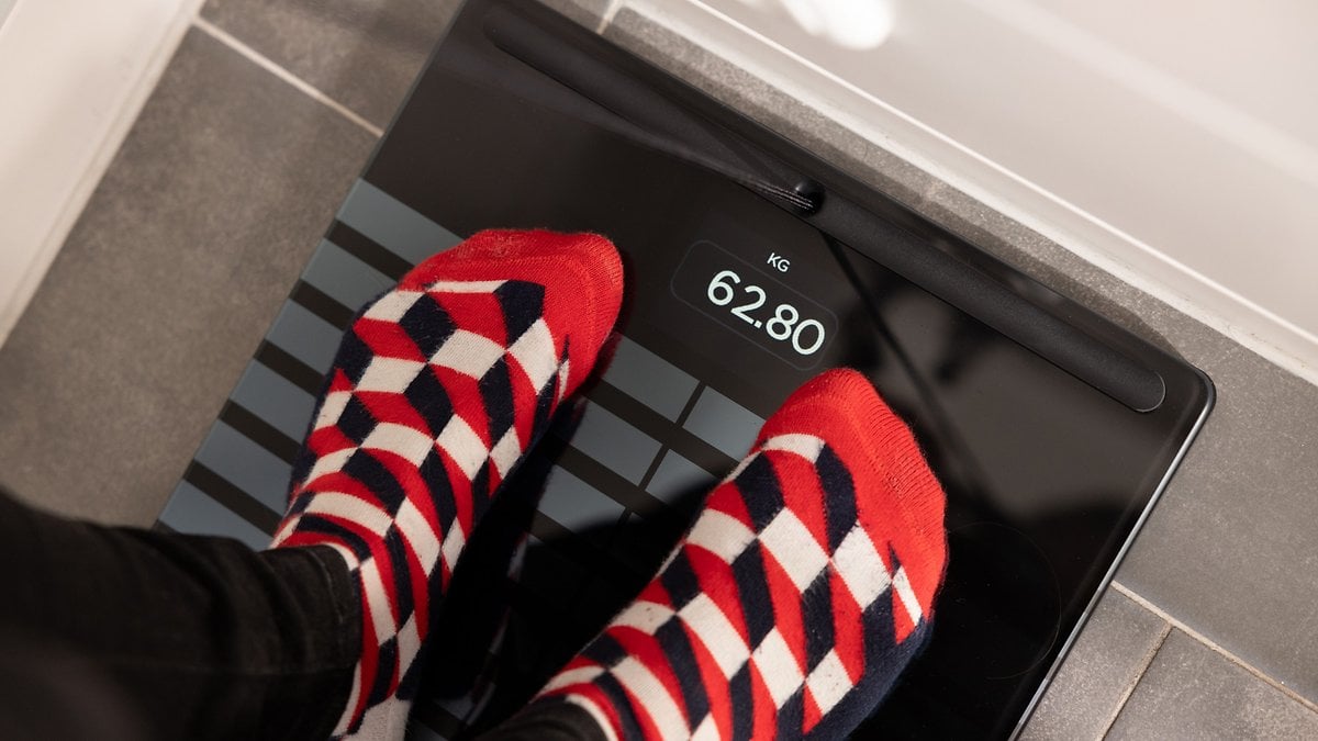 Des pieds avec des chaussettes à motifs rouges et blancs sur une balance Withings Body Scan affichant 62,80 kg.