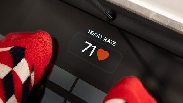 A person's feet in patterned socks on a scale displaying a heart rate of 71.