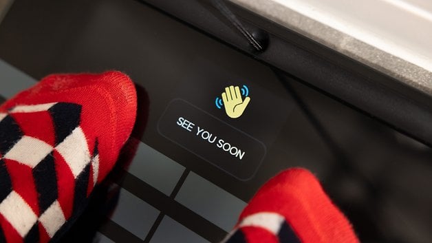 A close-up of feet in red and blue socks on a smart scale displaying 'SEE YOU SOON'.