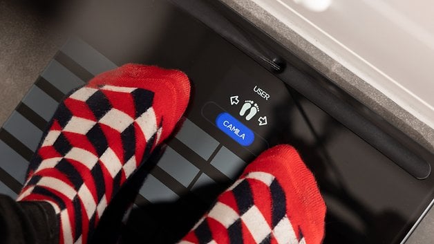 Feet in colorful socks standing on a Withings body scan scale display.