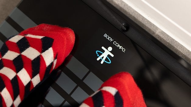 Feet in red and white patterned socks on a Withings body composition scale displaying 'BODY COMPO.'