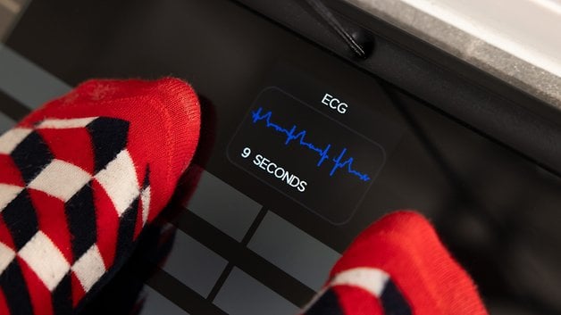 Feet in colorful socks on a digital scale displaying 'ECG' and '9 SECONDS'.