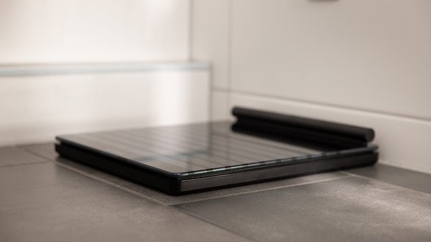 A sleek black Withings Body Scan scale on a tiled floor.