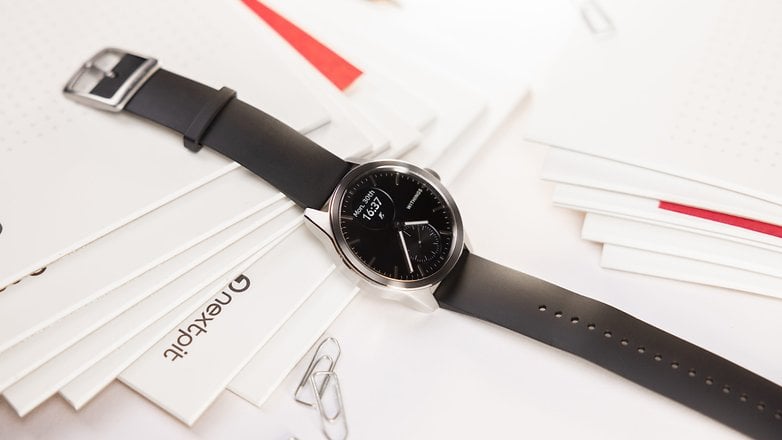 Withings Smartwatch 2 zeigt die Zeit in analoger und digitaler Form an und steht auf einem Stapel Papierblätter.