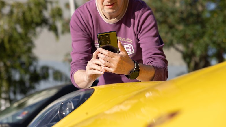 Matt penché sur le capot d'une voiture jaune tenant le Xiaomi 13T Pro dans ses deux mains