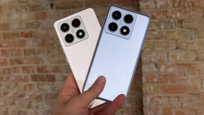 Deux smartphones Xiaomi dans une main devant un mur en briques.