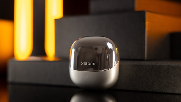 Étui de chargement des Xiaomi Buds 5 sur des surfaces sombres avec un fond lumineux chaud.