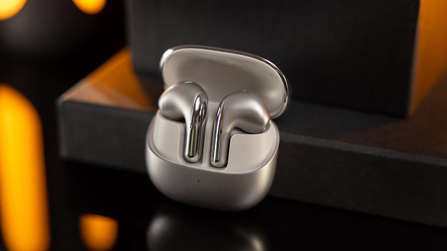 Xiaomi Buds 5 dans leur étui de chargement, présentés sur une surface sombre avec un éclairage chaleureux.