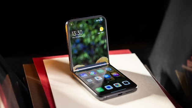 Ein Xiaomi Mix Flip Smartphone wird geöffnet und zeigt einen bunten Startbildschirm auf einem Stapel