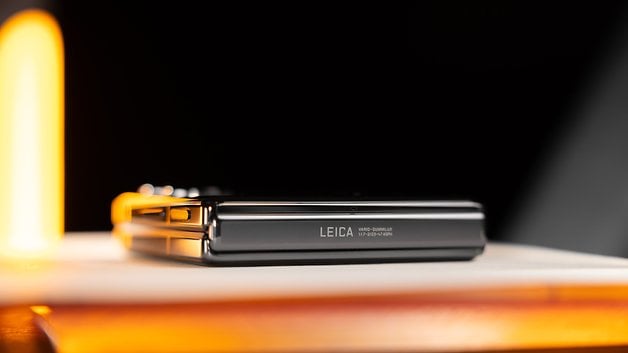 Smartphone Xiaomi Mix Flip avec marque Leica, posé sur une surface avec un éclairage chaud.