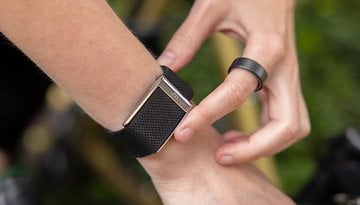 A person adjusting an Oura Ring on their wrist, wearing a black mesh band and a simple black ring.