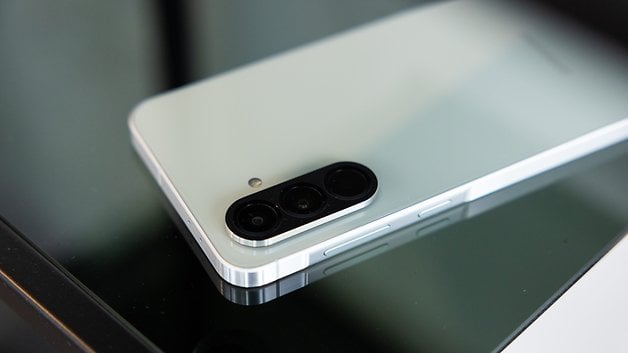 Un smartphone Samsung Galaxy A56 posé sur une surface en verre, montrant son module de caméra et son design épuré.