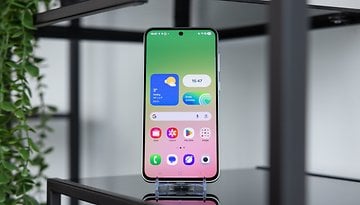 A Samsung Galaxy A series smartphone on a stand, displaying a colorful home screen with widgets.