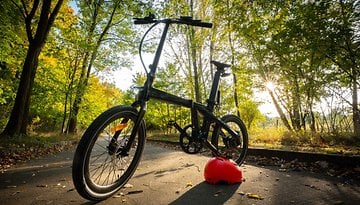 Ein schwarzes Fahrrad mit dünnen Reifen und einem roten Helm, der auf einem Weg umgeben von Bäumen im Herbst ruht.