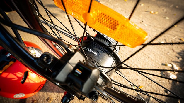 Nahaufnahme eines Fahrradhub mit schwarzem Gehäuse und orangefarbenen Reflektoren, daneben ein roter Helm.