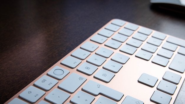 Close-up de um teclado Apple com teclas cinza claro sobre uma superfície de madeira.