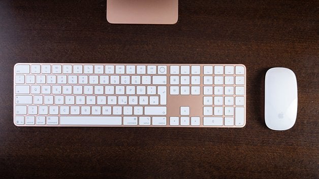 Teclado e mouse Apple em uma superfície de madeira, com design elegante e teclas brancas.