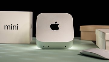 Apple Mac Mini M4 2024 on a surface with a mouse and boxes in the background.