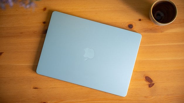 Um MacBook Air azul claro da Apple repousando sobre uma mesa de madeira ao lado de uma xícara.