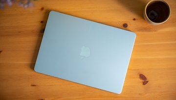 A light blue Apple MacBook Air resting on a wooden table next to a cup.
