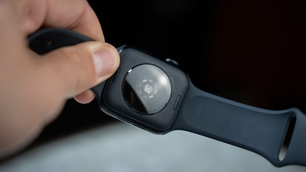 A person holds an Apple Watch SE 3 and shows the back with sensors and a black strap.