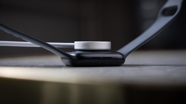 Apple Watch SE 3 charging on a surface with a black strap and silver charger. Apple Watch SE 3 charging on a surface with a black strap and silver charger.