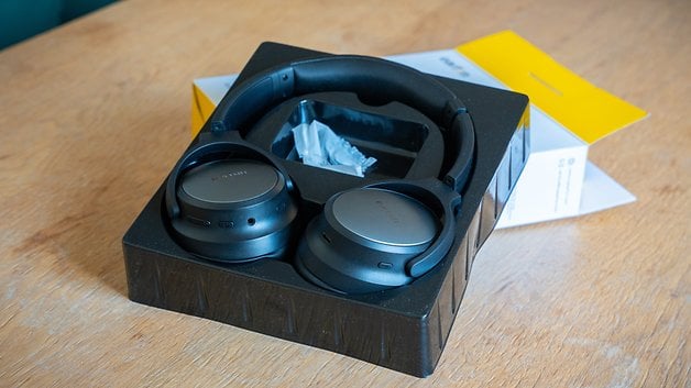Black over-ear headphones in its ANC works via several microphones placepackaging on a wooden table.