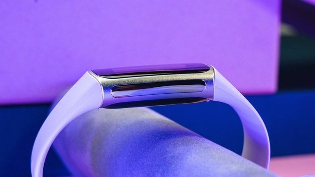 A Fitbit Charge 6 fitness tracker with a white band, displayed on a colorful background.