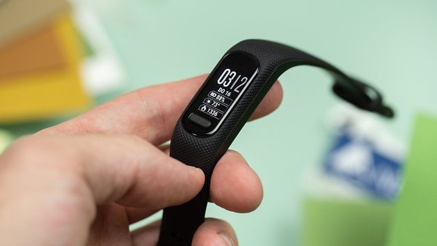 A person holding a Garmin Vivosmart 5 fitness band displaying time and activity data.