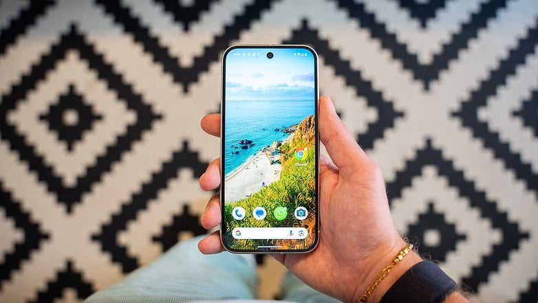 A hand holding a Google Pixel 9 smartphone displaying a beach wallpaper.