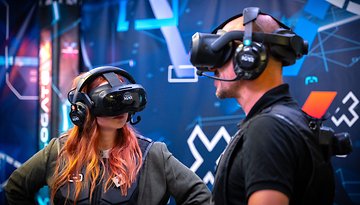 Two people wearing VR headsets engage in a virtual reality experience against a digital backdrop.