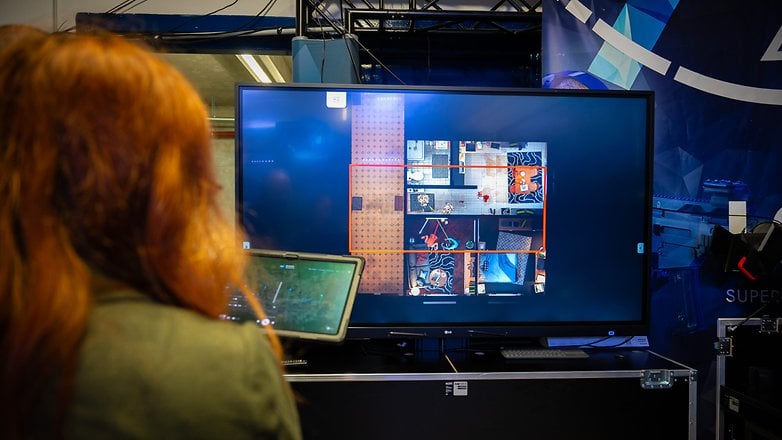 A person with red hair using a laptop in front of a large screen displaying a holodeck layout.