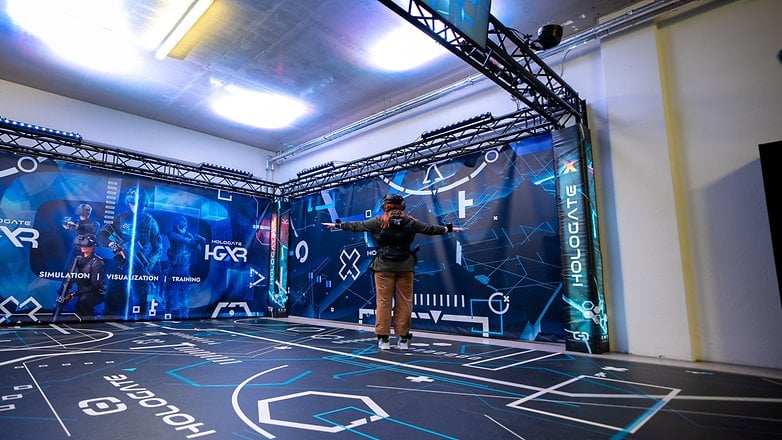 A person wearing VR gear stands in a Hologate simulation space with digital graphics on walls and floor.