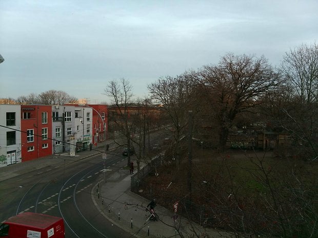 Blick auf eine Straße mit bunten Gebäuden, Bäumen und einem Park in einem Wohngebiet.