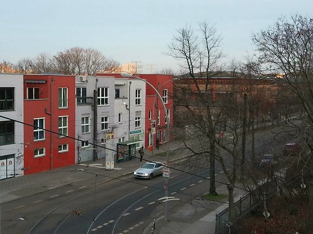 Eine Ansicht einer Straße mit Gebäuden, Bäumen und einem silbernen Auto an einem bewölkten Tag.