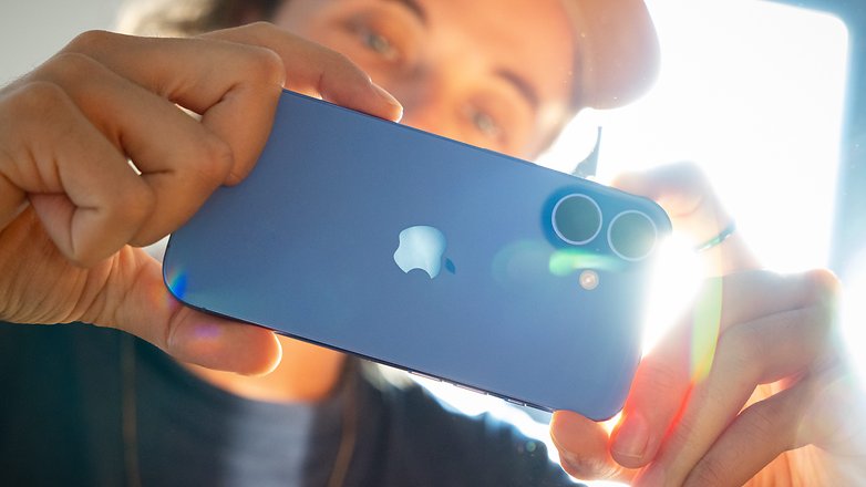 A person holding an Apple iPhone 16, showcasing its blue color and dual camera setup.