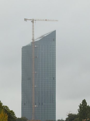 Ein hoher Glasturm im Bau mit einem Kran an der Spitze an einem bewölkten Tag.